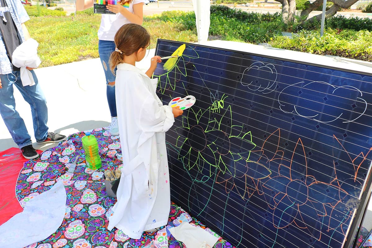 Student painting flowers, the sun and sky on a solar panel